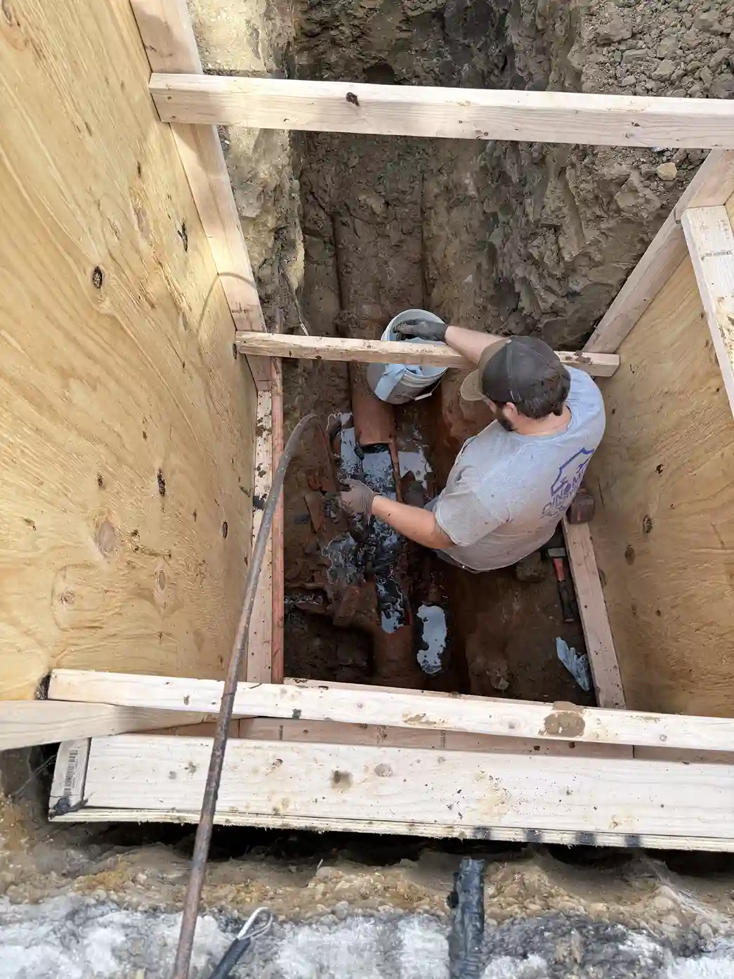 Plumber repairing sewer line in trench