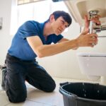 Male Plumber Fixing Leak In Domestic Bathroom Sink Or Basin