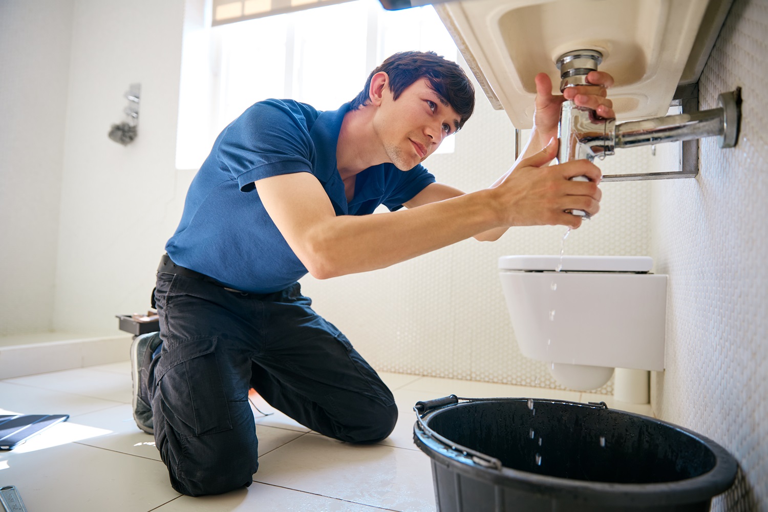 Male Plumber Fixing Leak In Domestic Bathroom Sink Or Basin