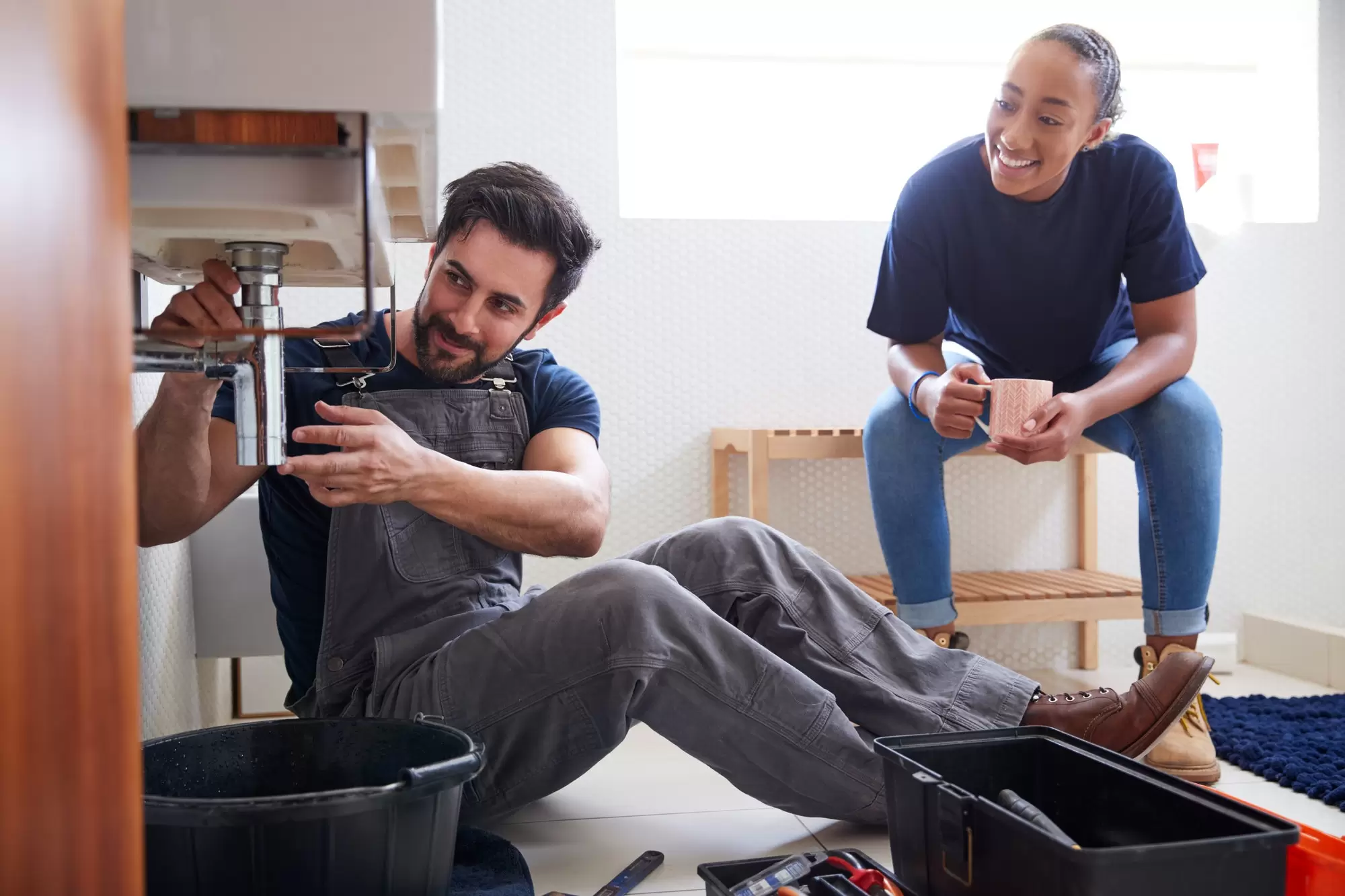 Plumber fixing a sink while homeowner watches