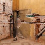 Exposed plumbing pipes installed inside damaged, broken brick and plaster walls during a home renovation or whole-house repiping project.